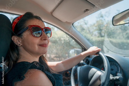 latin woman in a car at steering wheel looking at camera © oscargutzo