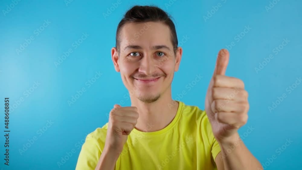 Young man at the camera and showing thumb up. Hot offer, summer days. Blue background. Slow motion Young man at the camera and showing thumb up. Hot offer, summer days. Blue background. Slow motion