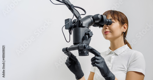 Woman dentist with innovative dental microscope on white background. Banner for dental theme. Concept of modern equipment for tooth treatment, professional clinic. Photo with free copy space.