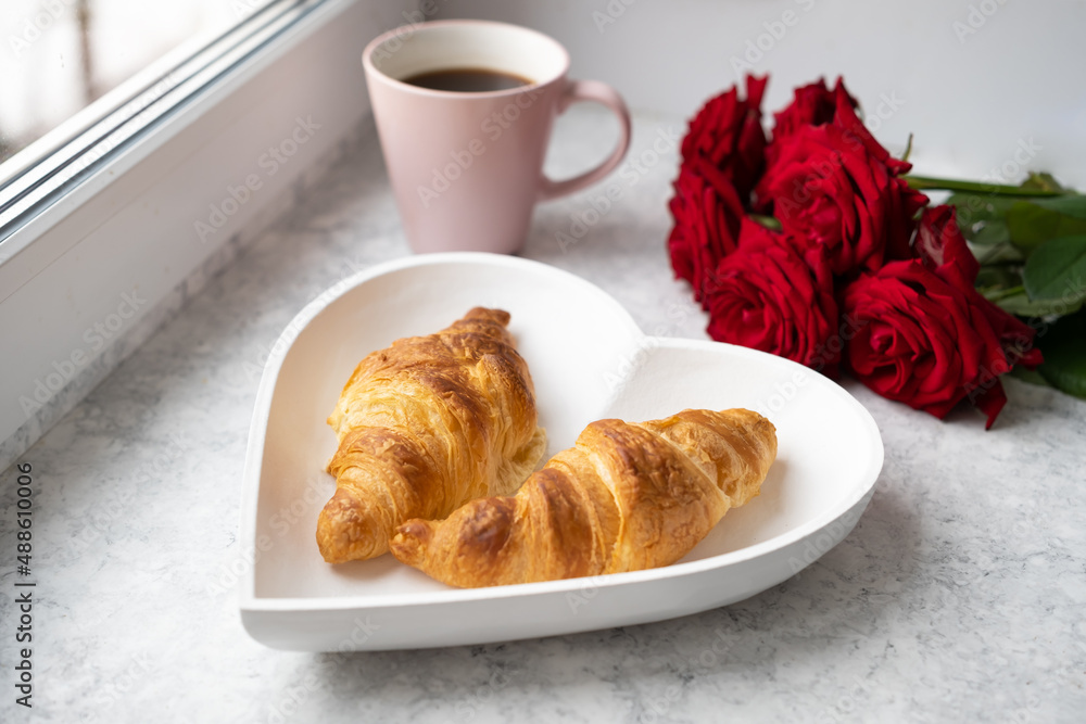 Beautiful romantic breakfast.French croissants on white heart-shaped plate , roses and cup of coffee on windowsill. Close-up.Valentine day,love or dating concept Beautiful romantic breakfast.French croissants on white heart-shaped plate , roses and cup of coffee on windowsill. Close-up.Valentine day,love or dating concept