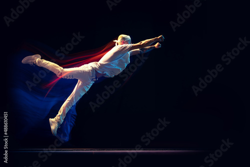 Portrait of man in sports white suit, hip-hop dancer flying isolated on dark background in mixed neon light. Youth culture, hip-hop, movement, style and fashion, action.