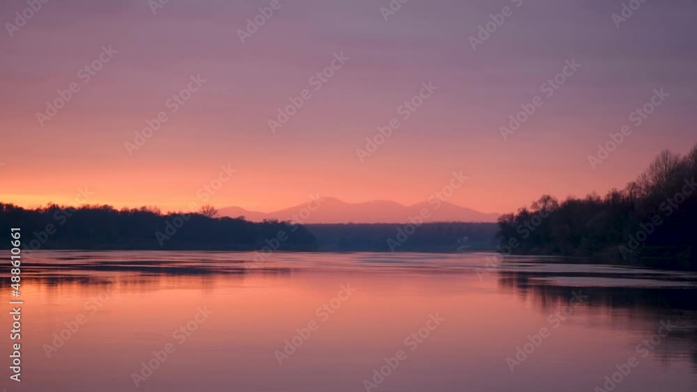 River with forest silhouette on shore and mountain in glowing haze at dusk River with forest silhouette on shore and mountain in glowing haze at dusk