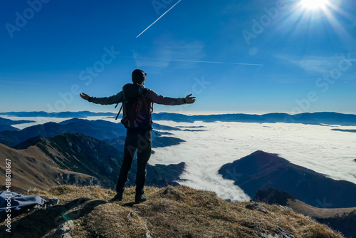 Man spreading his arms over a panoramic view from mount Eisenerzer Reichenstein in Styria, Austria, Europe. The Ennstal valley is covered in clouds. Hiking trail, Wanderlust. Sunny day.Freedom concept