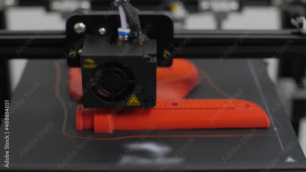 The printing mechanism adds layers to an orange 3D object. Three-dimensional