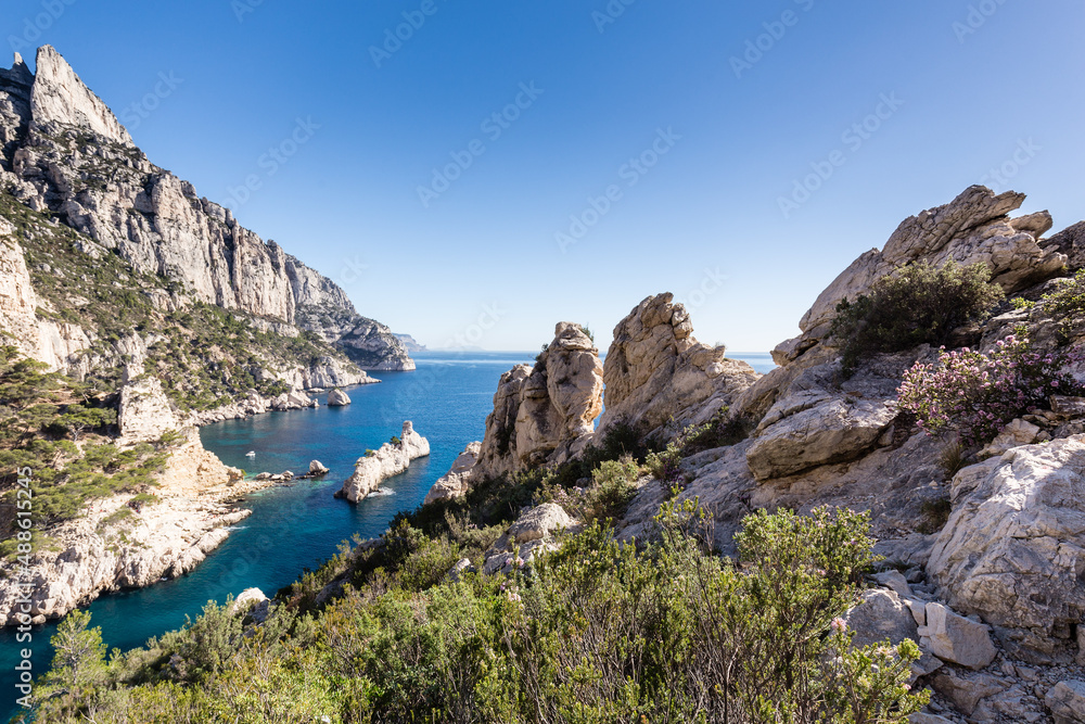 Crique de méditerranée étroite aux eaux pures et bleues entourée de falaises calcaires à pic avec un îlot en forme de sous-marin. Calanque de Sugiton, Le Torpilleur.