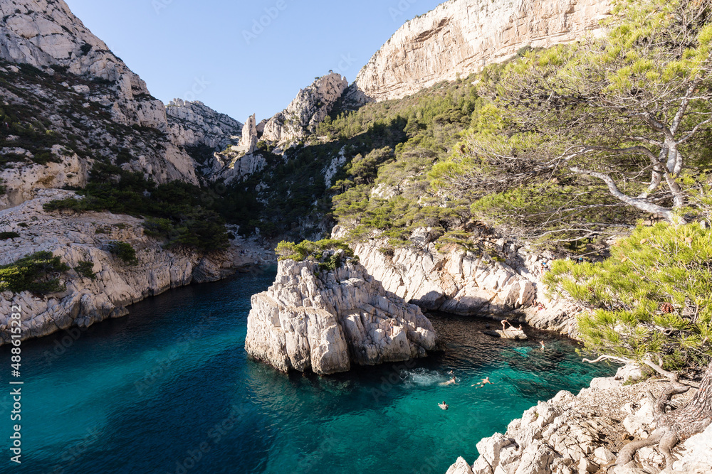 Petite crique aux eaux transparentes et turquoises avec baigneurs au soleil, entourée de falaises calcaires et de pins. Méditerranée, Calanque de Sugiton, France