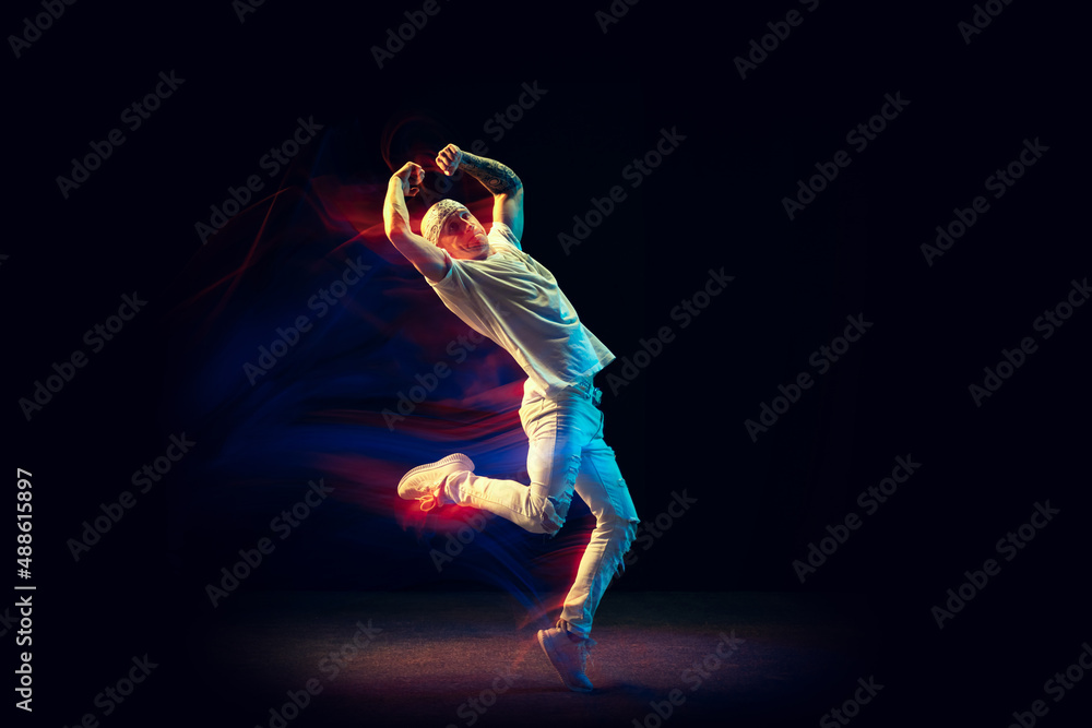 Freedom. Flexible man in white jeans and tee dancing hip-hop isolated on dark background in mixed neon light. Youth culture, street style and fashion, action.