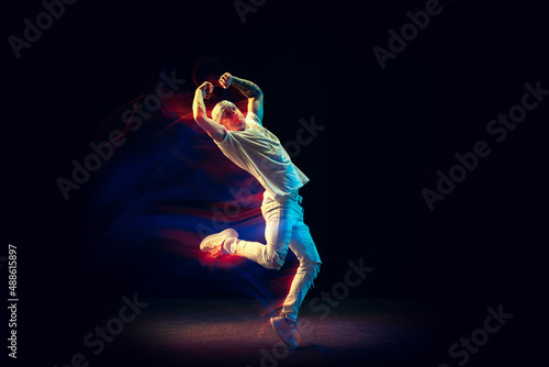 Freedom. Flexible man in white jeans and tee dancing hip-hop isolated on dark background in mixed neon light. Youth culture, street style and fashion, action.