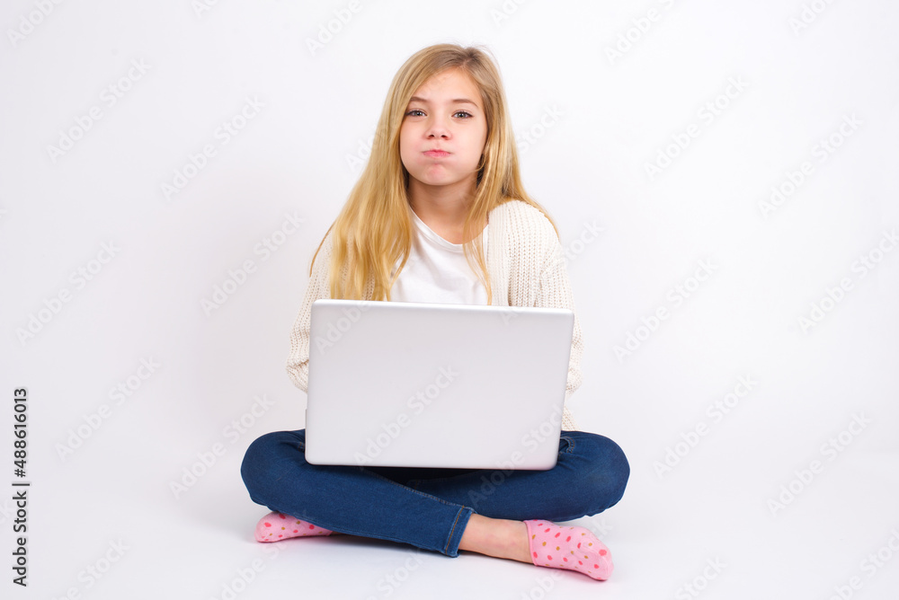 caucasian teen girl sitting with laptop in lotus position on white background puffing cheeks with funny face. Mouth inflated with air, crazy expression. caucasian teen girl sitting with laptop in lotus position on white background puffing cheeks with funny face. Mouth inflated with air, crazy expression.