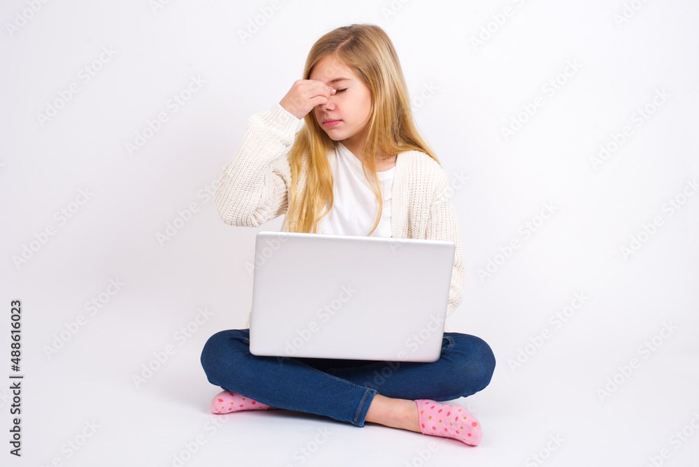Very upset, caucasian teen girl sitting with laptop in lotus position on white background touching nose between closed eyes, wants to cry, having stressful relationship or having troubles with work Very upset, caucasian teen girl sitting with laptop in lotus position on white background touching nose between closed eyes, wants to cry, having stressful relationship or having troubles with work