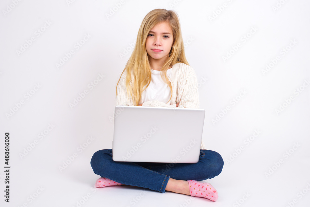 caucasian teen girl sitting with laptop in lotus position on white background bitting his mouth and looking worried and scared crossing arms, worry and doubt. caucasian teen girl sitting with laptop in lotus position on white background bitting his mouth and looking worried and scared crossing arms, worry and doubt.