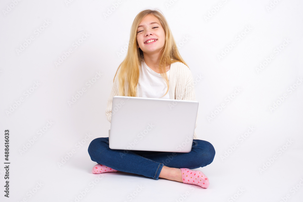 caucasian teen girl sitting with laptop in lotus position on white background with broad smile, shows white teeth, feeling confident rejoices having day off. caucasian teen girl sitting with laptop in lotus position on white background with broad smile, shows white teeth, feeling confident rejoices having day off.