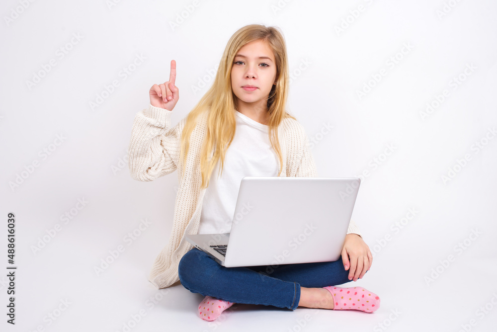caucasian teen girl sitting with laptop in lotus position on white background showing and pointing up with fingers number one while smiling confident and happy. caucasian teen girl sitting with laptop in lotus position on white background showing and pointing up with fingers number one while smiling confident and happy.