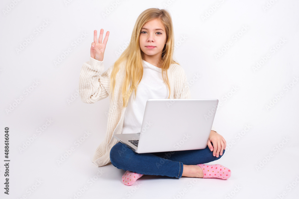 caucasian teen girl sitting with laptop in lotus position on white background showing and pointing up with fingers number three while smiling confident and happy. caucasian teen girl sitting with laptop in lotus position on white background showing and pointing up with fingers number three while smiling confident and happy.