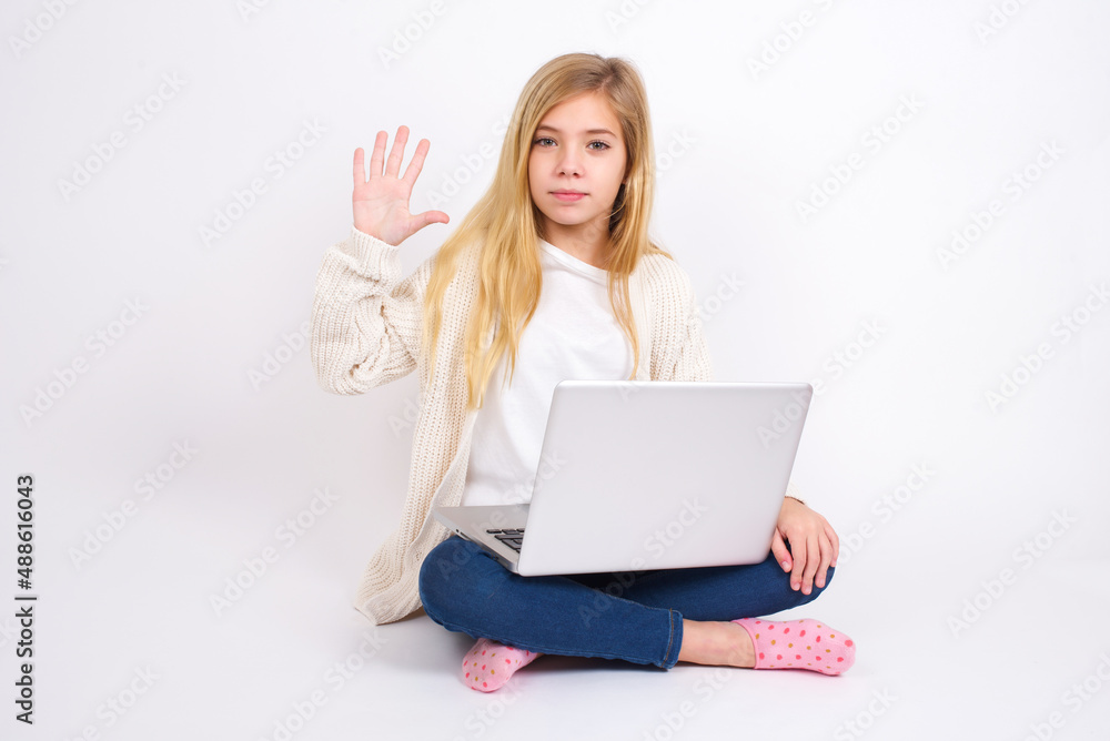 caucasian teen girl sitting with laptop in lotus position on white background showing and pointing up with fingers number five while smiling confident and happy. caucasian teen girl sitting with laptop in lotus position on white background showing and pointing up with fingers number five while smiling confident and happy.