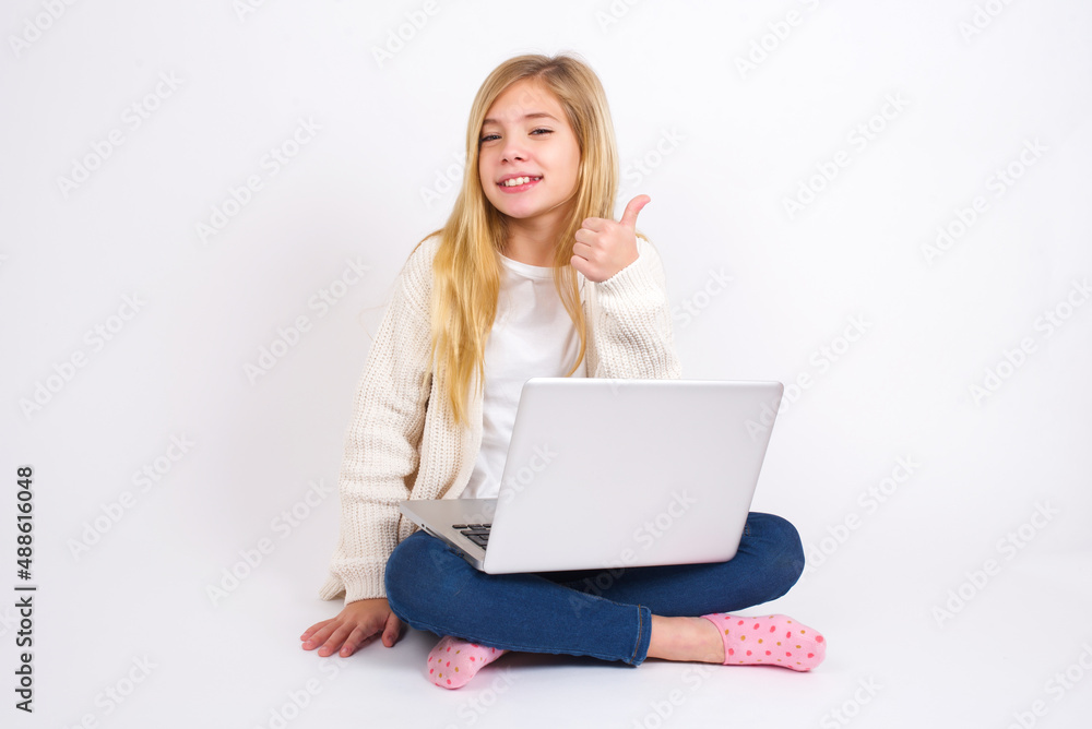 caucasian teen girl sitting with laptop in lotus position on white background giving thumb up gesture, good Job! Positive human emotion facial expression body language. caucasian teen girl sitting with laptop in lotus position on white background giving thumb up gesture, good Job! Positive human emotion facial expression body language.