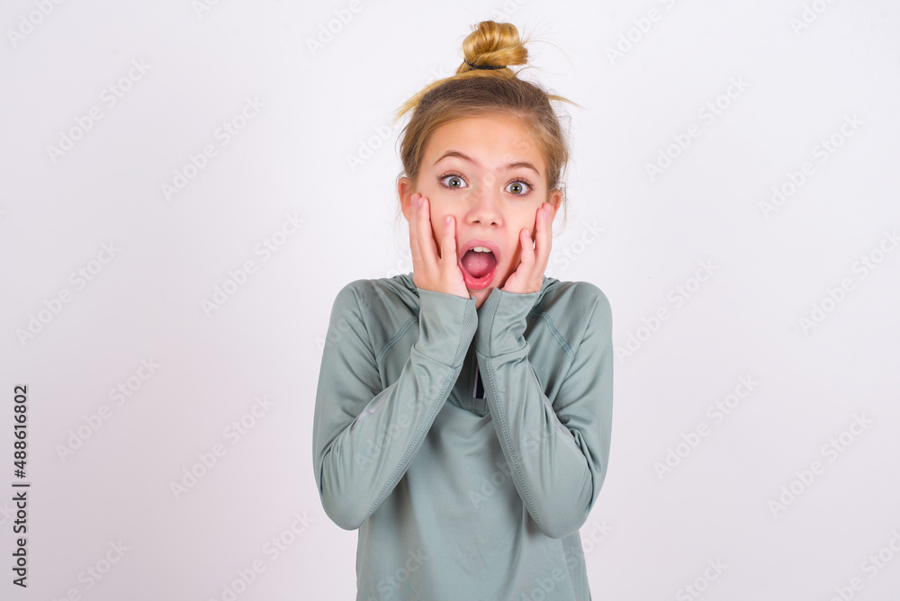 Stupefied little caucasian kid girl with hair bun wearing technical ...