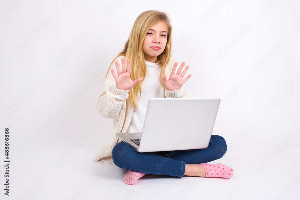 caucasian teen girl sitting with laptop in lotus position on white background doing stop sing with palm of the hand. Warning expression with negative and serious gesture on the face. caucasian teen girl sitting with laptop in lotus position on white background doing stop sing with palm of the hand. Warning expression with negative and serious gesture on the face.