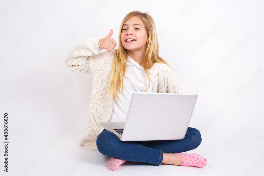 caucasian teen girl sitting with laptop in lotus position on white background imitates telephone conversation, makes phone call gesture with hands, has confident expression. Call me! caucasian teen girl sitting with laptop in lotus position on white background imitates telephone conversation, makes phone call gesture with hands, has confident expression. Call me!