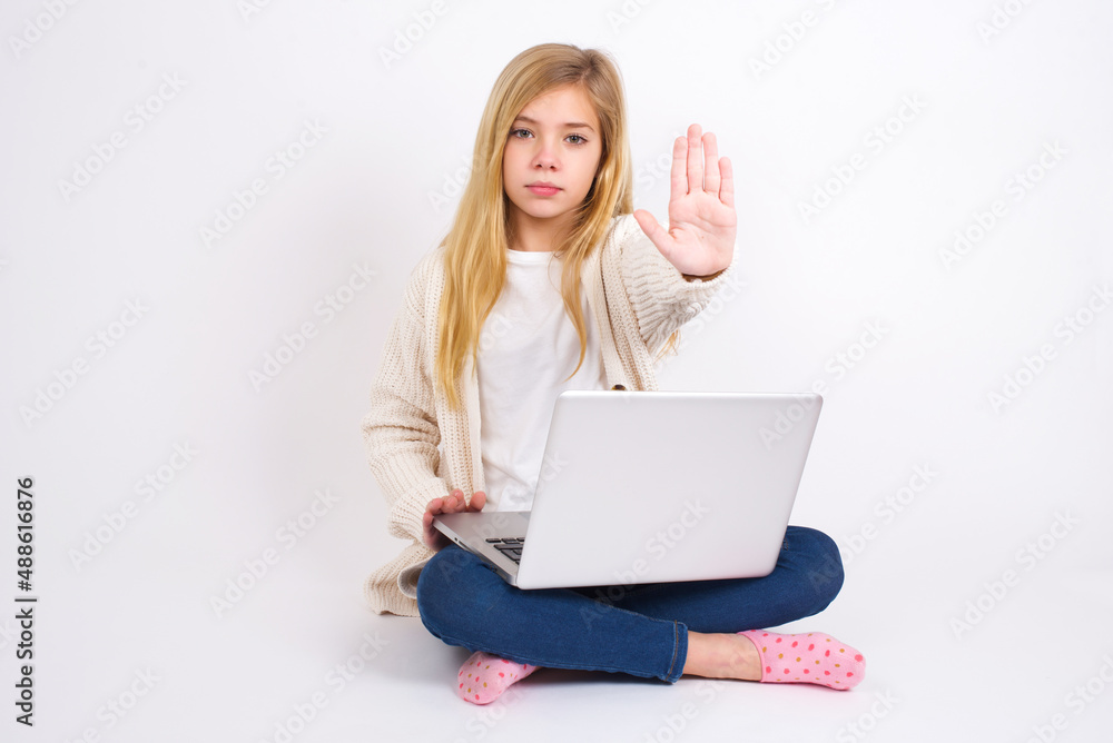 caucasian teen girl sitting with laptop in lotus position on white background doing stop gesture with palm of the hand. Warning expression with negative and serious gesture on the face. caucasian teen girl sitting with laptop in lotus position on white background doing stop gesture with palm of the hand. Warning expression with negative and serious gesture on the face.