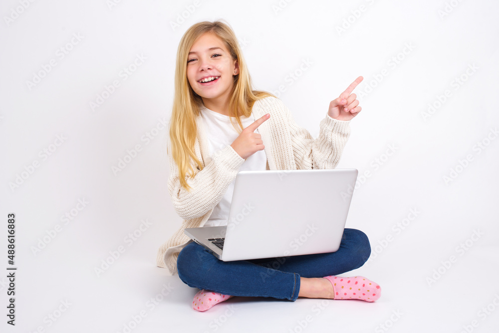 caucasian teen girl sitting with laptop in lotus position on white background with positive expression, indicates with fore finger at blank copy space for your promotional text or advertisement. caucasian teen girl sitting with laptop in lotus position on white background with positive expression, indicates with fore finger at blank copy space for your promotional text or advertisement.