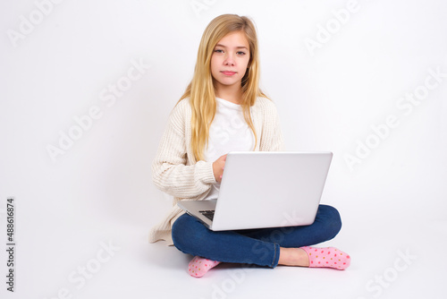 Business Concept - Portrait of caucasian teen girl sitting with laptop in lotus position on white background holding hands with confident face. © Jihan