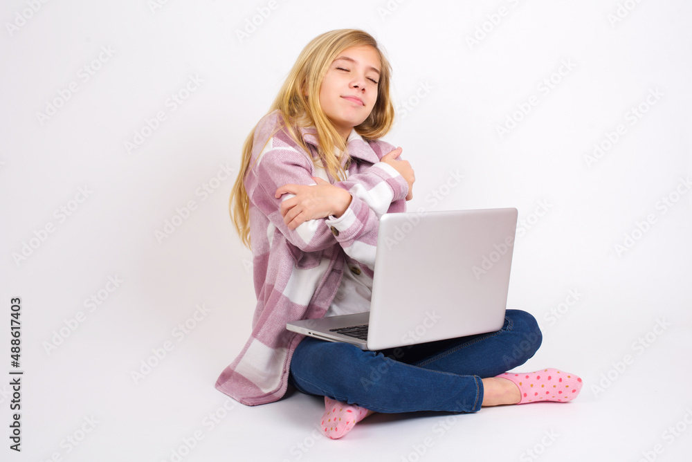 caucasian teen girl sitting with laptop in lotus position on white background . Hugging oneself happy and positive, smiling confident. Self love and self care. caucasian teen girl sitting with laptop in lotus position on white background . Hugging oneself happy and positive, smiling confident. Self love and self care.