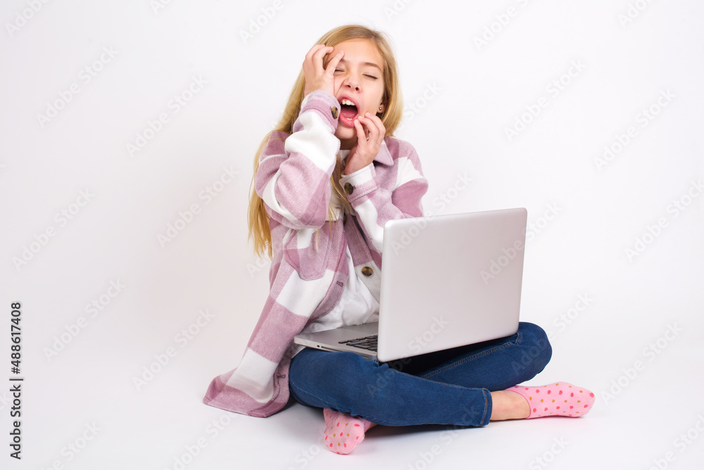 Young gloomy caucasian teen girl sitting with laptop in lotus position on white background , hiding face with hands pouting and crying, standing upset and depressed complaining about job problem. Young gloomy caucasian teen girl sitting with laptop in lotus position on white background , hiding face with hands pouting and crying, standing upset and depressed complaining about job problem.