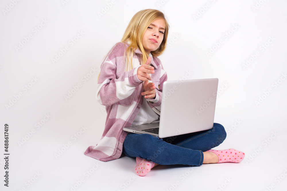 Hey you, bang. Joyful and charismatic good-looking caucasian teen girl sitting with laptop in lotus position on white background winking and pointing with finger pistols at camera happily and cheeky. Hey you, bang. Joyful and charismatic good-looking caucasian teen girl sitting with laptop in lotus position on white background winking and pointing with finger pistols at camera happily and cheeky.