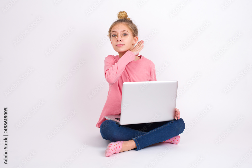 caucasian teen girl sitting with laptop in lotus position on white background cutting throat with hand as knife, threaten aggression with furious violence. caucasian teen girl sitting with laptop in lotus position on white background cutting throat with hand as knife, threaten aggression with furious violence.