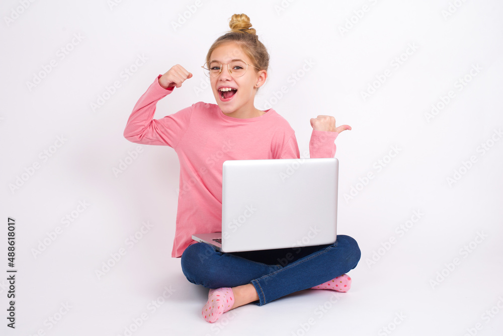 Hooray cool caucasian teen girl sitting with laptop in lotus position on white background point back empty space hand fist Hooray cool caucasian teen girl sitting with laptop in lotus position on white background point back empty space hand fist