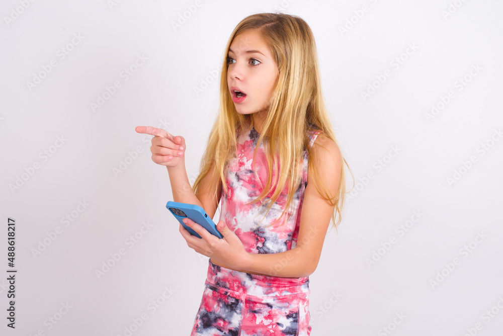 Stunned little caucasian kid girl wearing sport clothing over white background points sideways right copy space, recommends product, sees astonishing thing Stunned little caucasian kid girl wearing sport clothing over white background points sideways right copy space, recommends product, sees astonishing thing