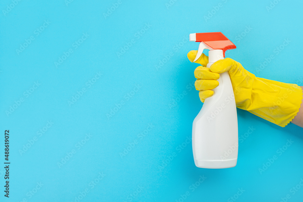 A hand in a yellow glove holds a white bottle of detergent on a blue background. Banner with copy space. Chemical cleaners, household chemicals, brushes and collage supplies. Cleaning concept. A hand in a yellow glove holds a white bottle of detergent on a blue background. Banner with copy space. Chemical cleaners, household chemicals, brushes and collage supplies. Cleaning concept.