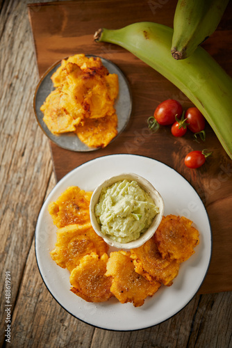 Patacones or tostones, typical Ecuadorian appetizer that consists on fried green plantain slices. It’s accompanied with guacamole and served on a traditional plate with a wooden and rustic background. photo