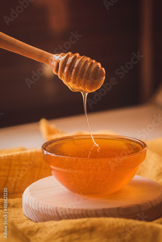 Honey dripping from honey dipper in bowl. Close-up. Healthy organic Thick honey dipping from the wooden honey spoon, closeup.