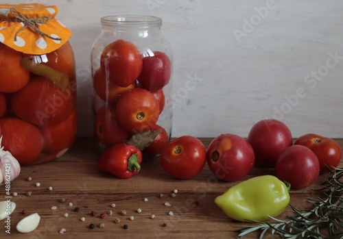 Red tomatoes with spices in glass jars and on a wooden surface.	