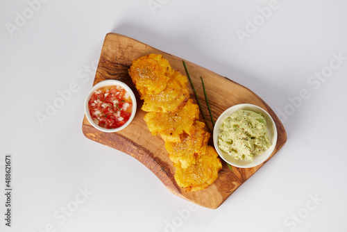 Patacones or tostones, typical Ecuadorian appetizer that consists on fried green plantain slices. It’s accompanied with guacamole and served on a traditional plate with a white background.  photo