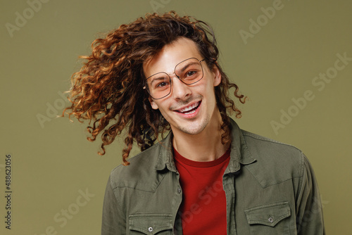 Close up smiling young brunet curly man 20s wears khaki shirt jacket glasses dance waving fooling around have fun enjoy play fluttering hair isolated on plain olive green background studio portrait.