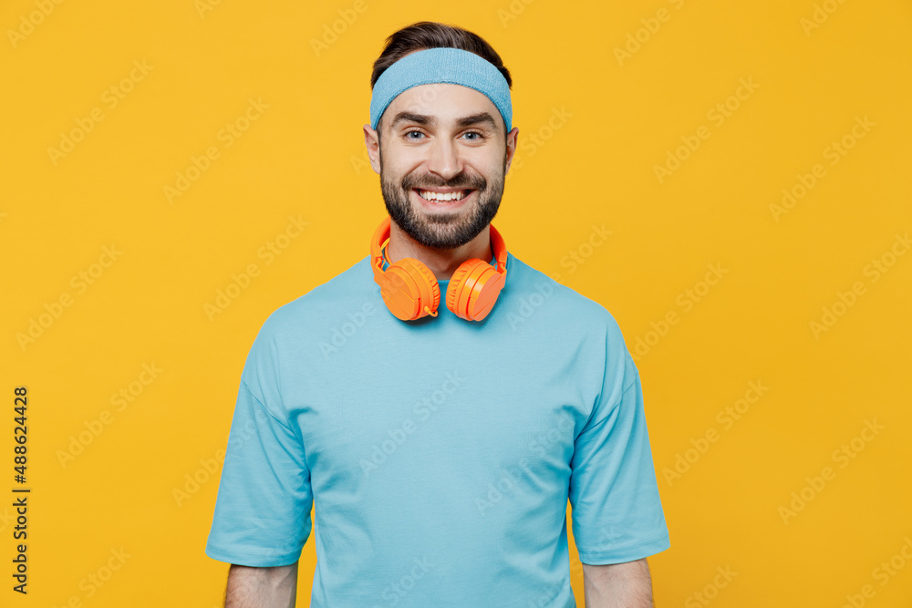 Young smiling happy fun fitness trainer instructor sporty man sportsman in headband blue t-shirt spend weekend in home gym isolated on yellow background. Workout sport motivation lifestyle concept Young smiling happy fun fitness trainer instructor sporty man sportsman in headband blue t-shirt spend weekend in home gym isolated on yellow background. Workout sport motivation lifestyle concept