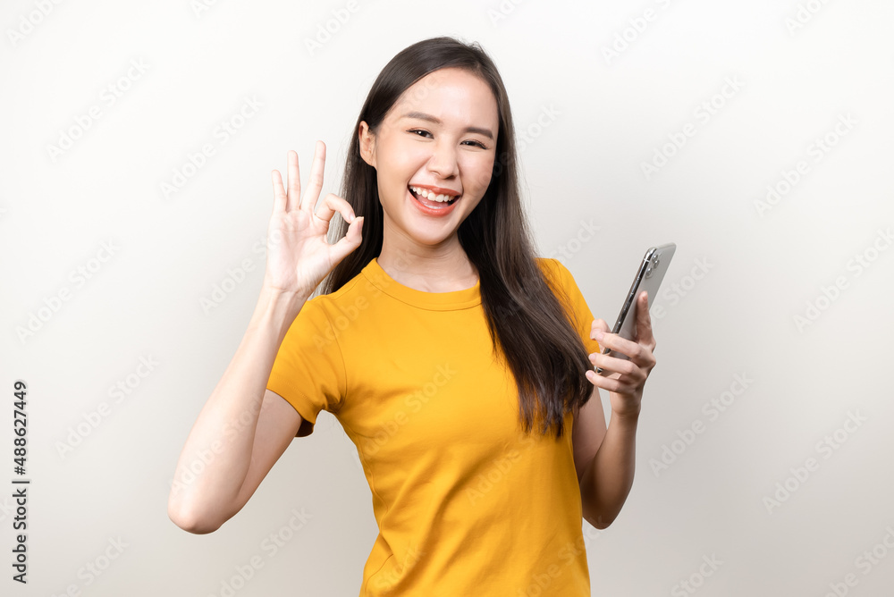 Happy asian woman holding smartphone and showing hand sign ok isolated on background Happy asian woman holding smartphone and showing hand sign ok isolated on background