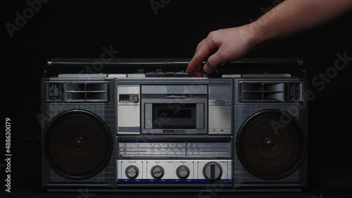 A man's hand inserts a cassette into a tape recorder and presses the play button