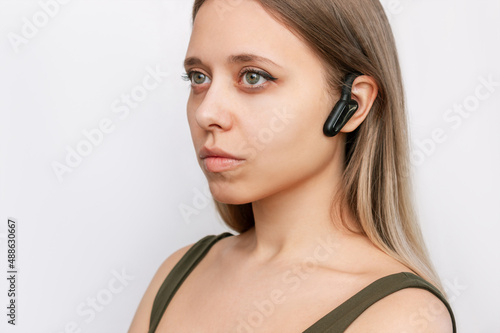 Portrait of a young attractive caucasian blonde woman listening to music in black wireless headphones with bone conduction for sports, running, cycling isolated on a white background