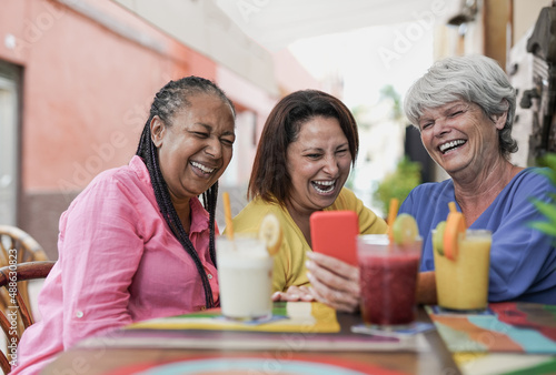 Senior multiracial women having fun at bar outdoor while using mobile phone