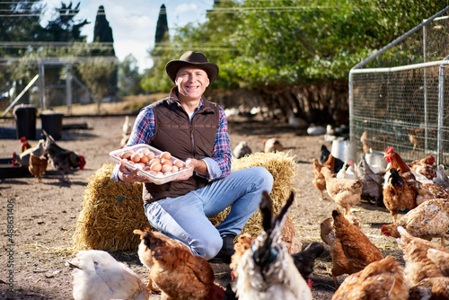 Man sits on the hay surrounded by chickens