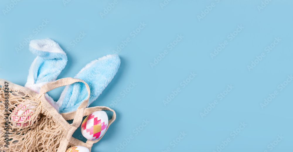 Wide banner on a blue background. The concept of online shopping for Easter, purchases and sale for the holiday. Gift bag with bunny ears and Easter eggs. Wide banner on a blue background. The concept of online shopping for Easter, purchases and sale for the holiday. Gift bag with bunny ears and Easter eggs.