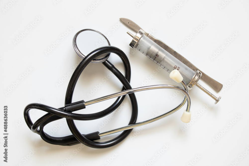 Stethoscope old syringe and scalpel lie on a white background ,medical instruments close up Stethoscope old syringe and scalpel lie on a white background ,medical instruments close up