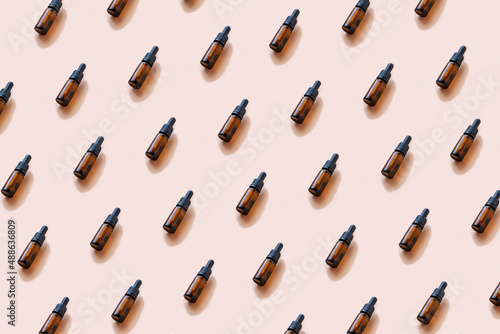 Repeating pattern from brown glass cosmetic or pharmaceutical bottles with dropper. Mockup, copy space, top view on coral background.