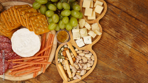 Different tasty appetizers on wooden background, top view. Snacks for wine. Cheese and meat plate. Sausages, cheese, nuts, grapes, crackers