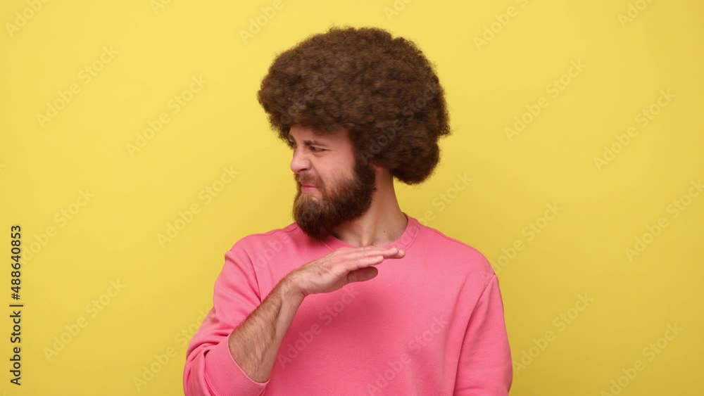 Man with Afro hairstyle holding breath with fingers on nose, grimacing in disgust, expressing repulsion to stink, fart gases, wearing pink sweatshirt. Indoor studio shot isolated on yellow background. Man with Afro hairstyle holding breath with fingers on nose, grimacing in disgust, expressing repulsion to stink, fart gases, wearing pink sweatshirt. Indoor studio shot isolated on yellow background.