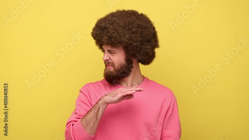 Man with Afro hairstyle holding breath with fingers on nose, grimacing in disgust, expressing repulsion to stink, fart gases, wearing pink sweatshirt. Indoor studio shot isolated on yellow background.